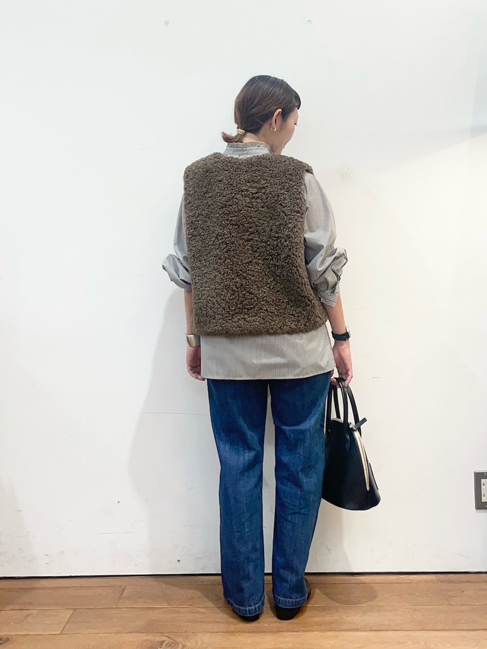 ブラック系のシャツ/ブラウス、ブラウン系のダウンベスト、ブルー系のデニムパンツを着用したレディースの秋コーディネートの5枚目の写真