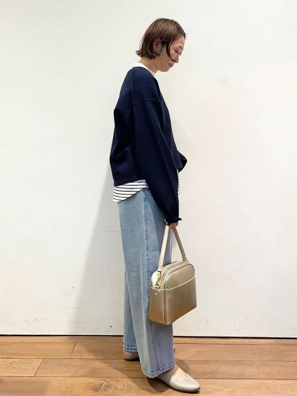 ゴールド系のショルダーバッグ、ブルー系のデニムパンツ、グレー系のパンプスを着用したレディースの冬コーディネートの4枚目の写真