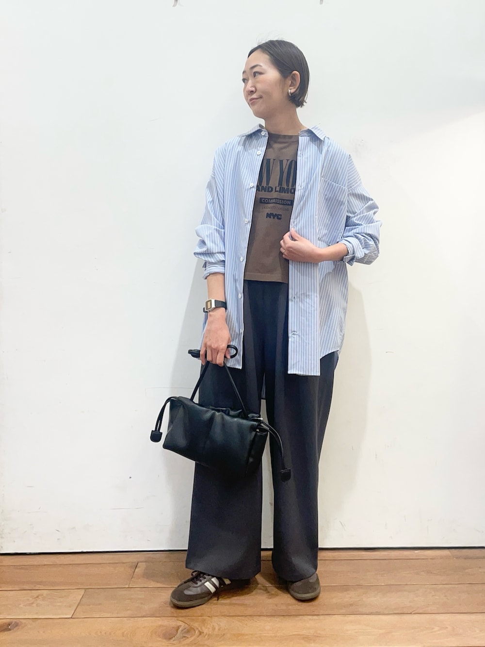 ブラック系のショルダーバッグ、ブルー系のシャツ/ブラウス、ブラウン系のTシャツ/カットソーを着用したレディースの春コーディネートの2枚目の写真