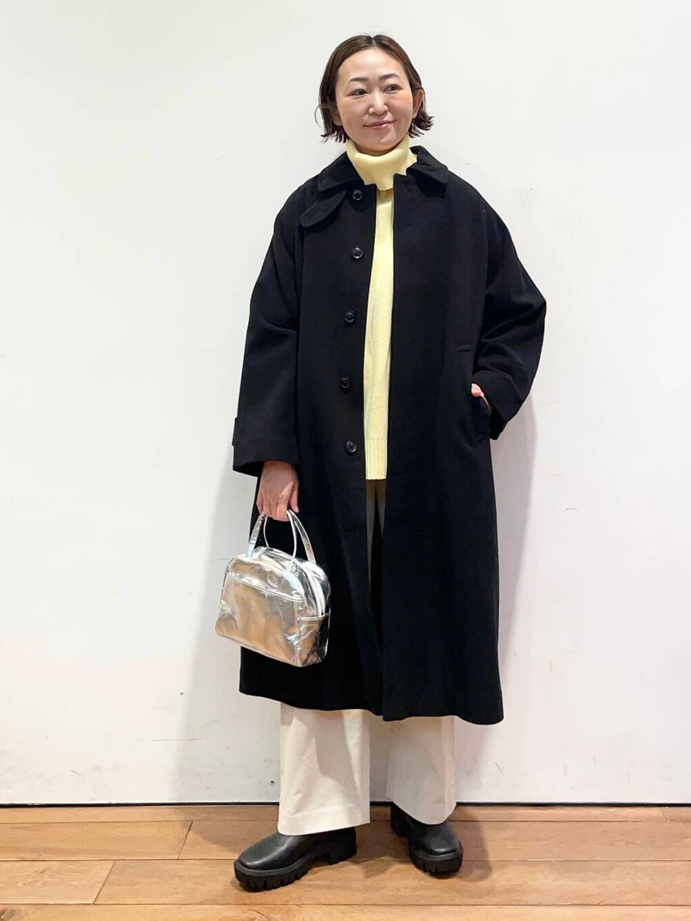 ブラック系のその他アウター、イエロー系のニット/セーター、ブラック系のブーツを着用したレディースの冬コーディネートの2枚目の写真