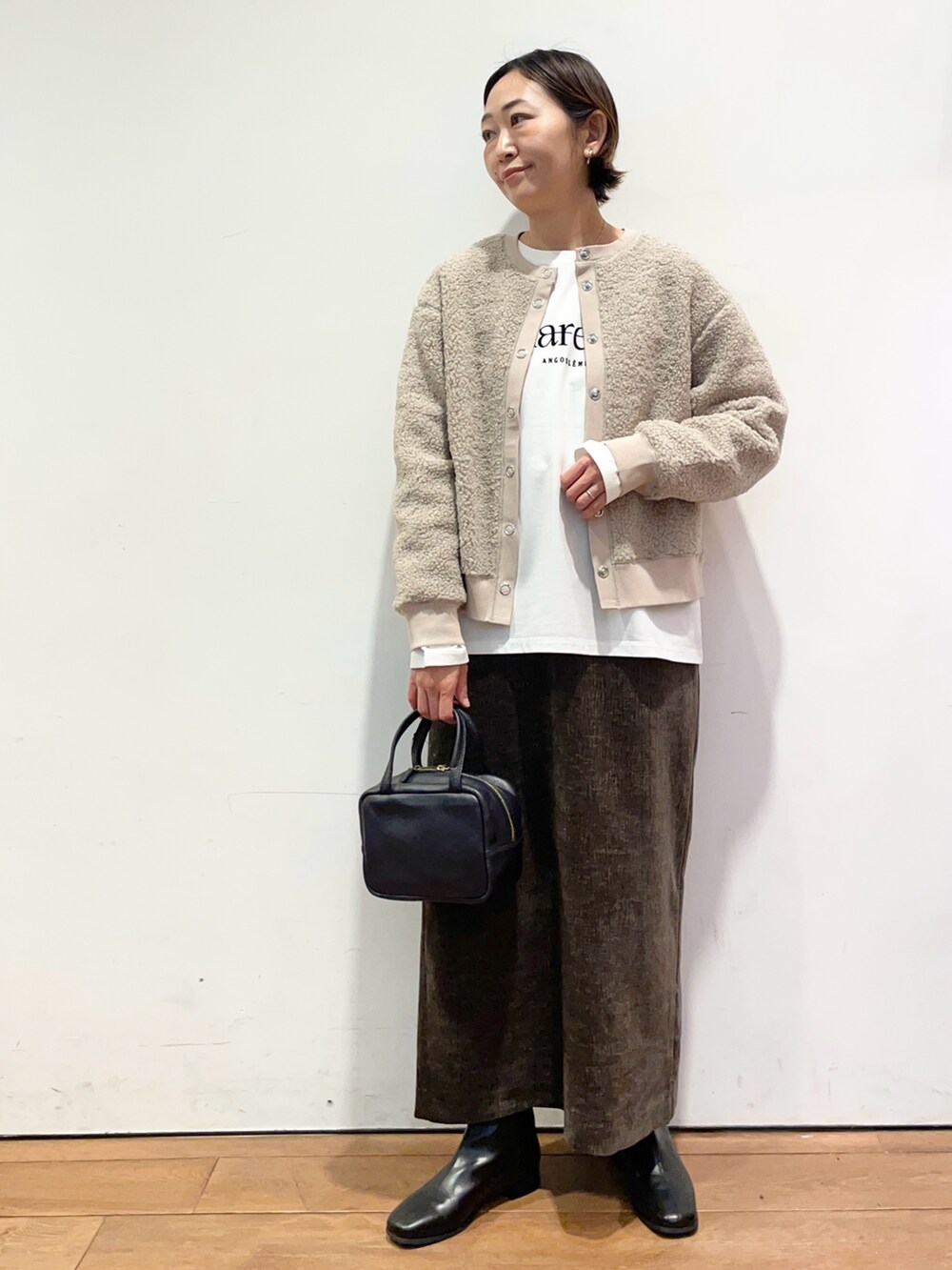 ホワイト系のTシャツ/カットソー、ベージュ系のカーディガン/ボレロ、ブラック系のブーツを着用したレディースの秋コーディネートの2枚目の写真