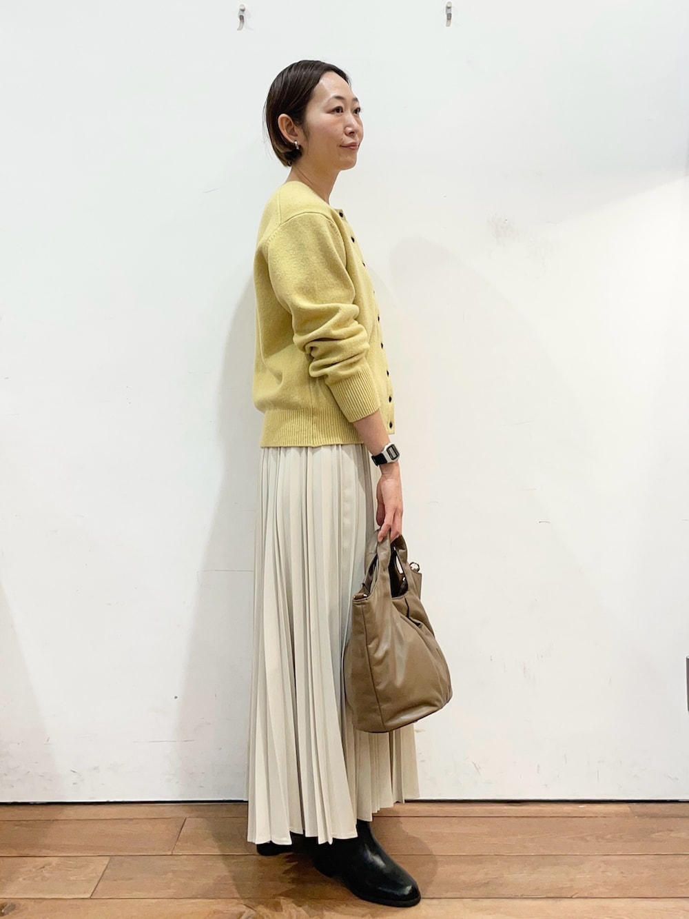 イエロー系のカーディガン/ボレロ、ホワイト系のスカート、ブラック系のブーツを着用したレディースの冬コーディネートの3枚目の写真