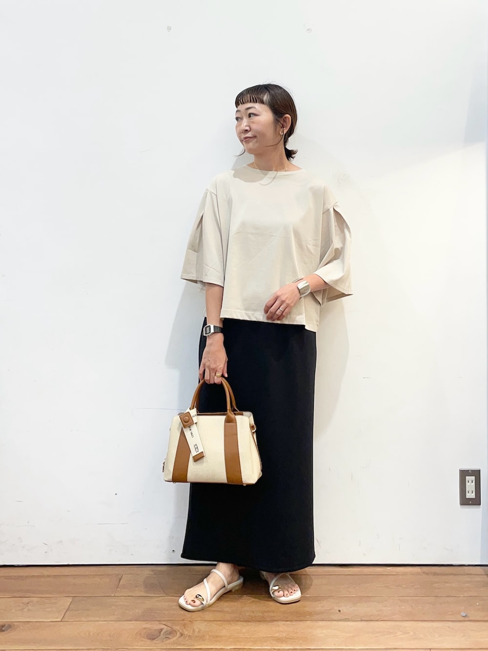 ベージュ系のTシャツ/カットソー、ブラック系のスカート、ホワイト系のハンドバッグを着用したレディースの夏コーディネートの2枚目の写真