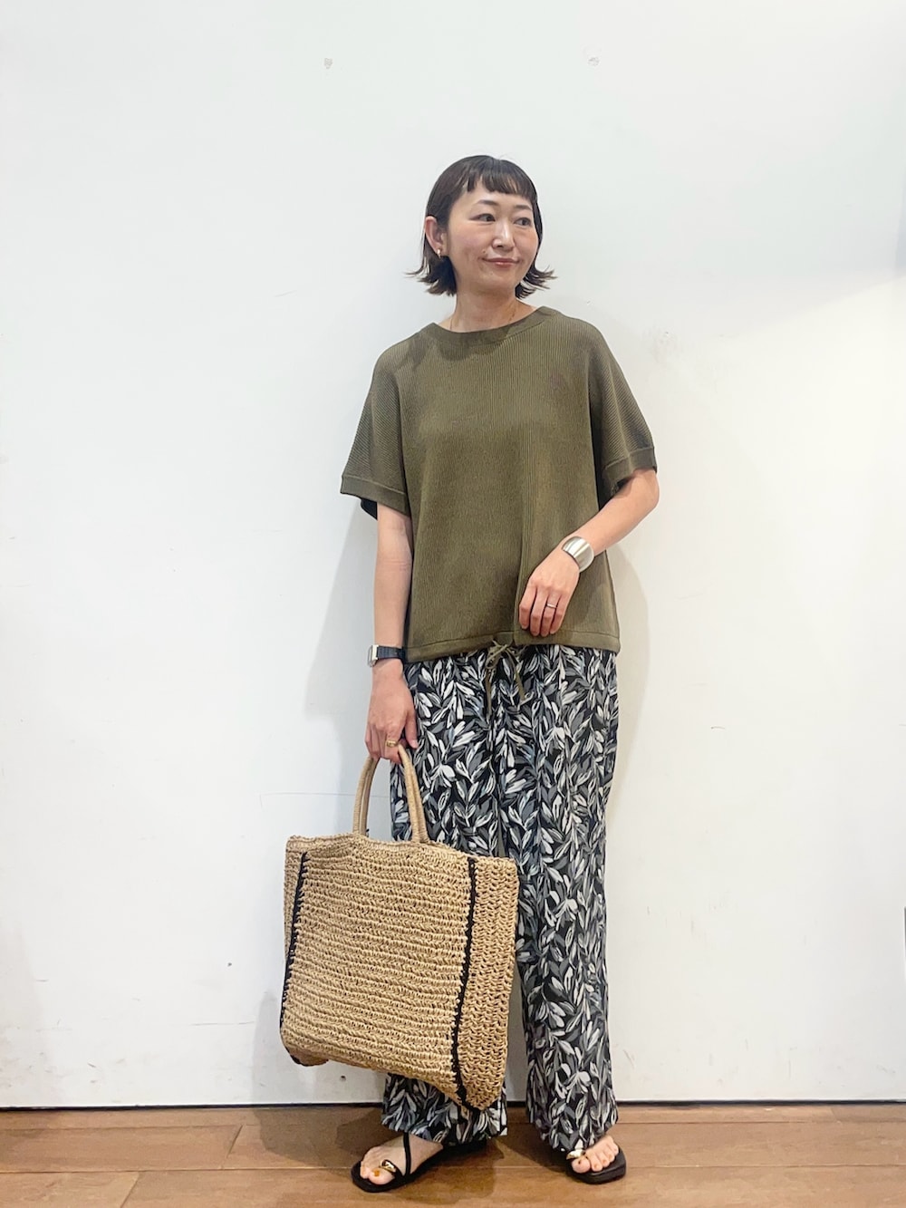 グリーン系のニット/セーター、ブラック系のその他パンツ、ベージュ系のトートバッグを着用したレディースの夏コーディネートの2枚目の写真