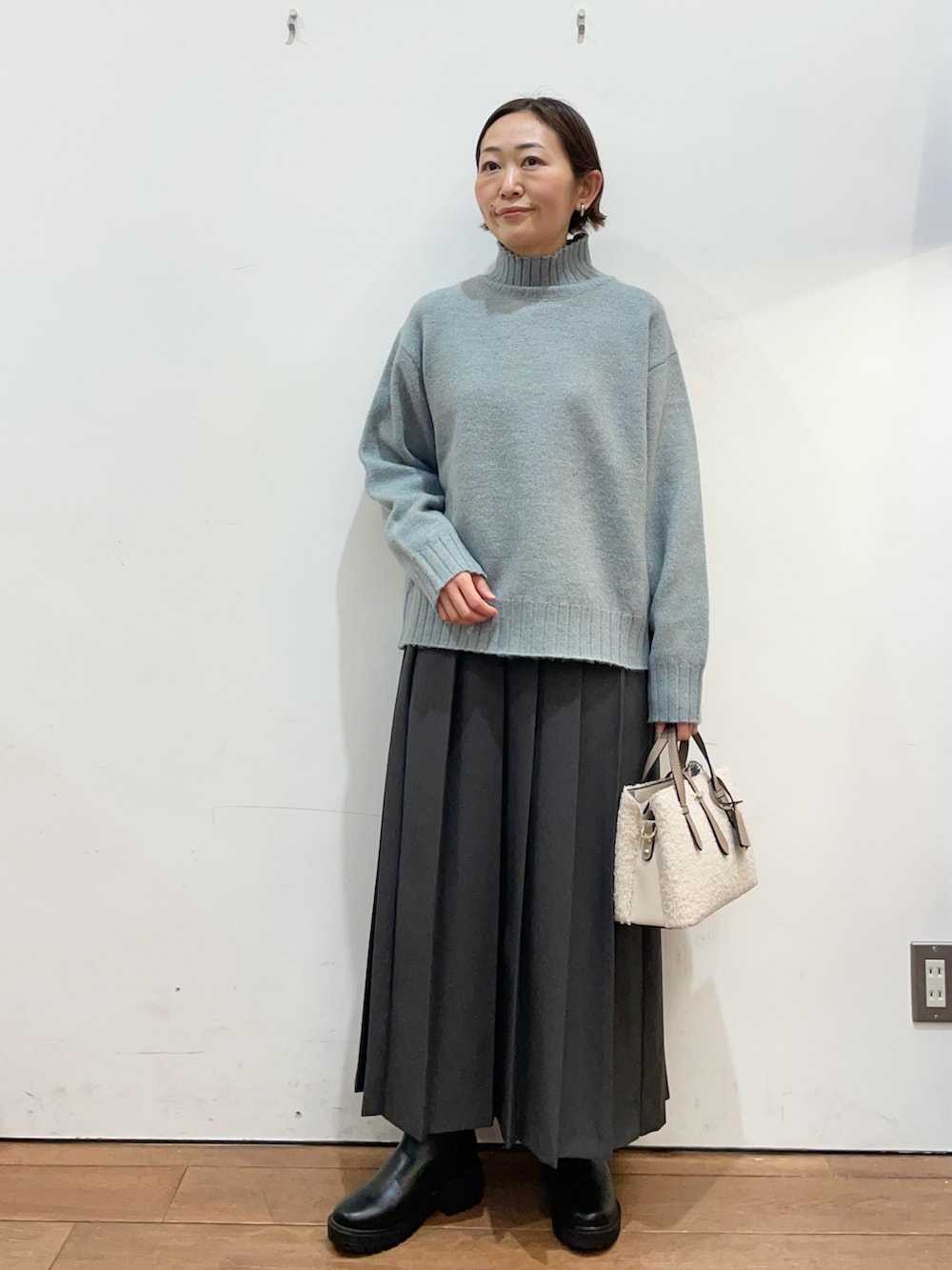 グリーン系のニット/セーター、グレー系のスカート、ブラック系のブーツを着用したレディースの冬コーディネートの2枚目の写真