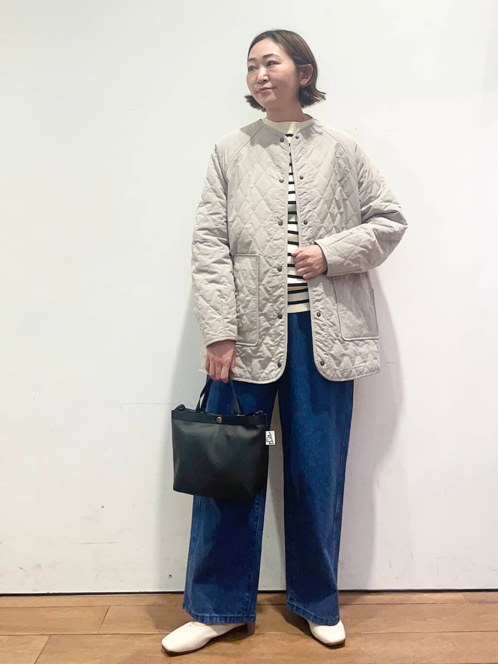 ブルー系のデニムパンツ、グレー系のダウンジャケット/コート、ブラック系のニット/セーターを着用したレディースの春コーディネートの3枚目の写真