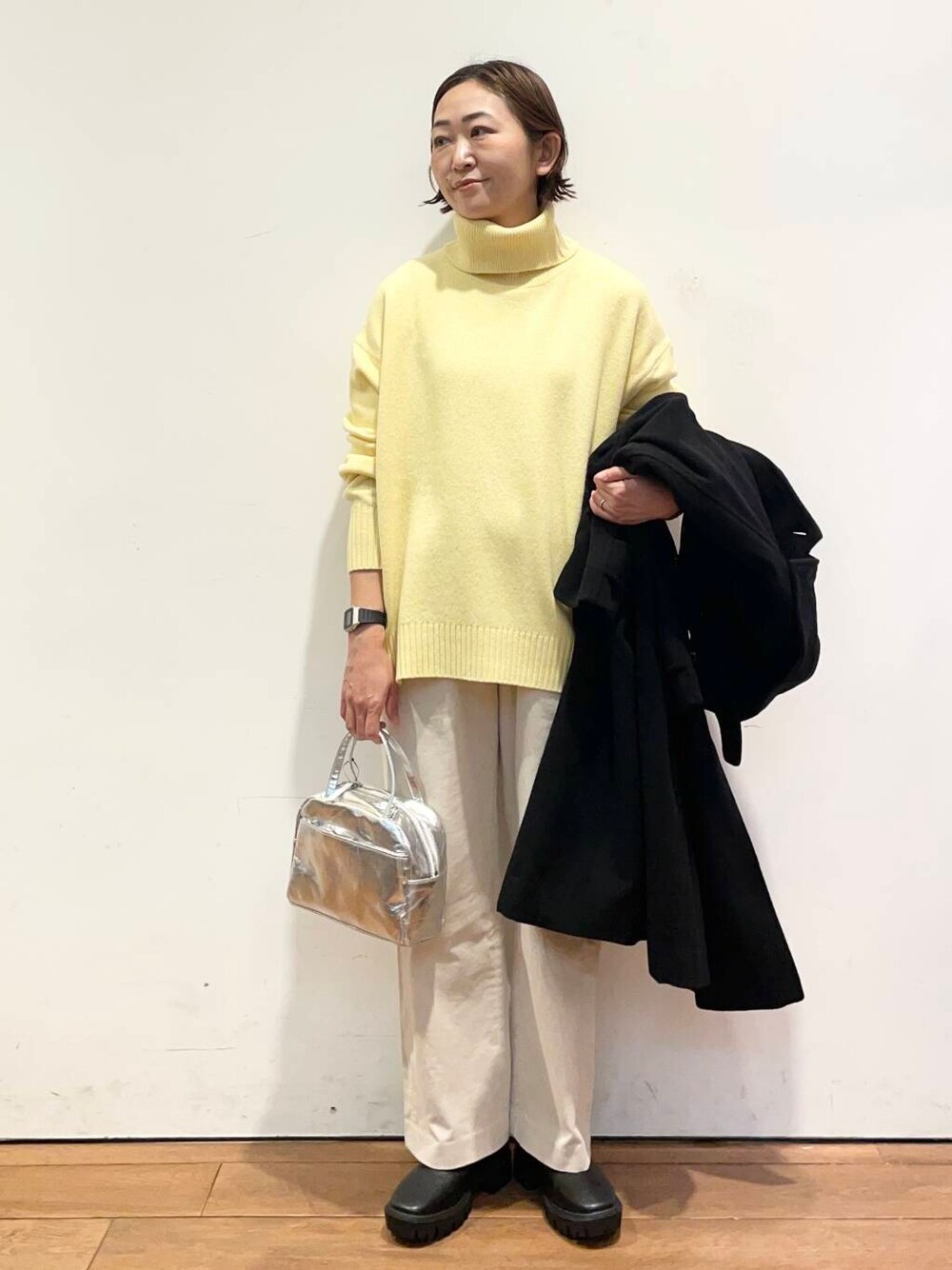 ブラック系のその他アウター、イエロー系のニット/セーター、ブラック系のブーツを着用したレディースの冬コーディネートの6枚目の写真