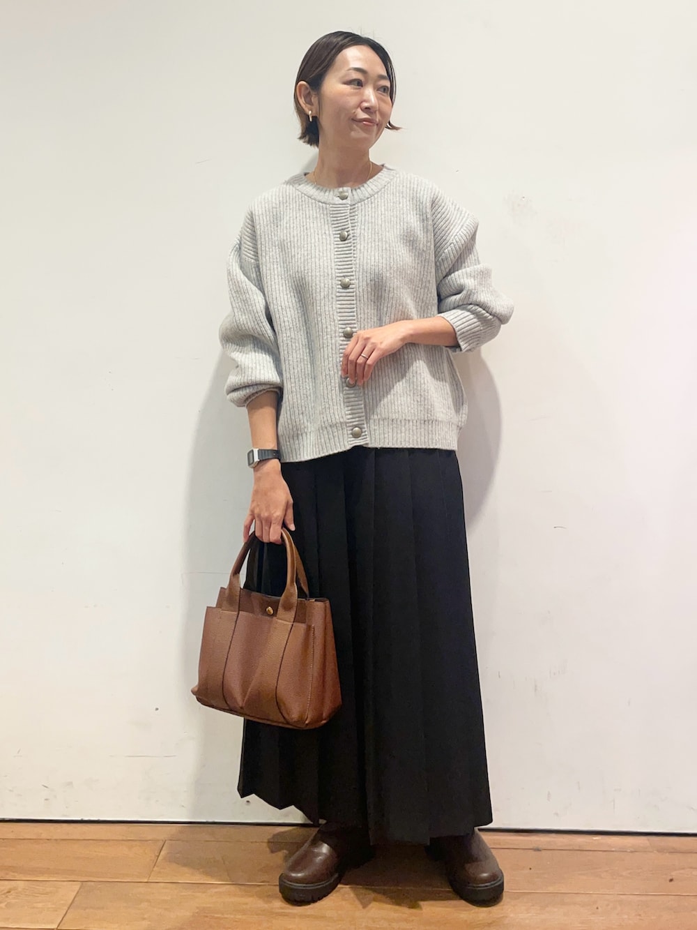 ブラック系のスカート、ブラウン系のトートバッグ、ブラウン系のブーツを着用したレディースの秋コーディネートの3枚目の写真