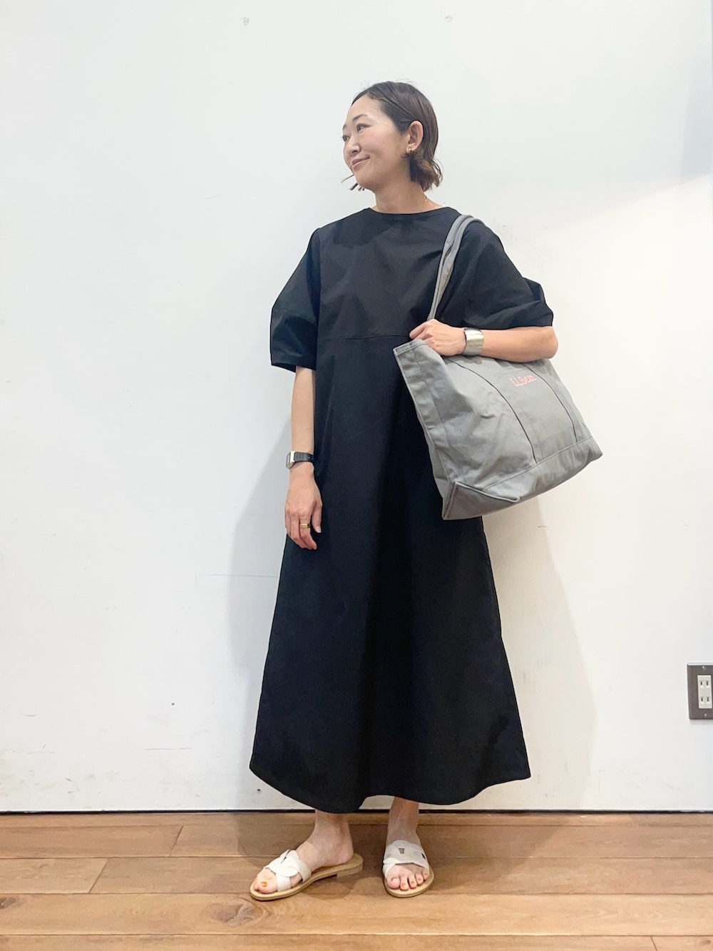 ブラック系のワンピース、ホワイト系のサンダル、グレー系のトートバッグを着用したレディースの春コーディネートの2枚目の写真