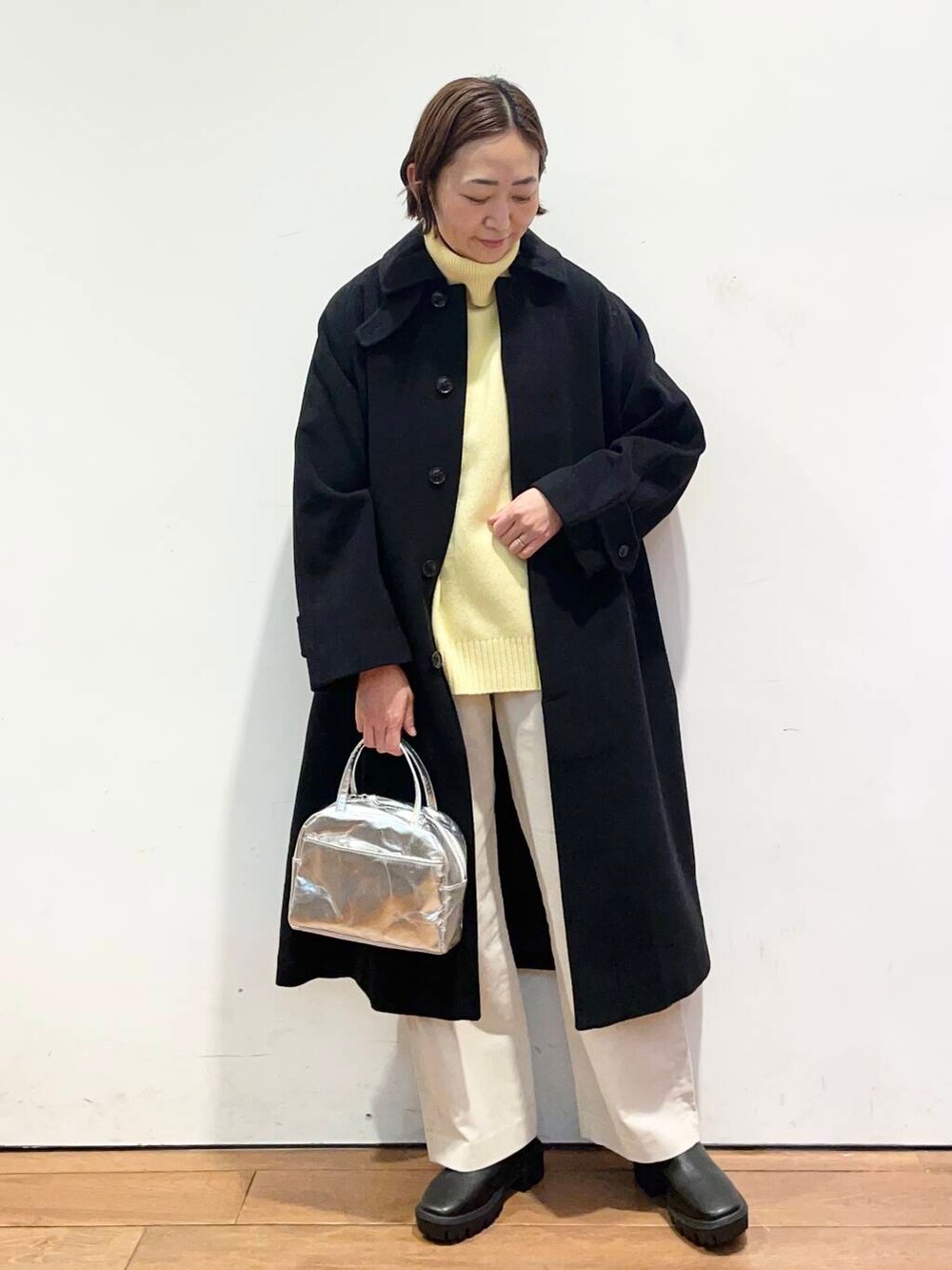 ブラック系のその他アウター、イエロー系のニット/セーター、ブラック系のブーツを着用したレディースの冬コーディネートの3枚目の写真