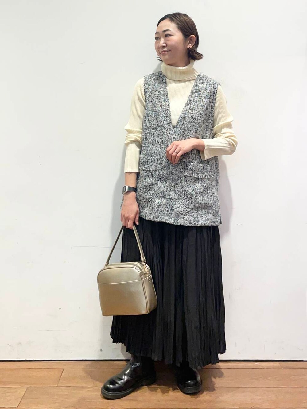 ゴールド系のショルダーバッグ、ホワイト系のニット/セーター、ブラック系のベストを着用したレディースの冬コーディネートの2枚目の写真