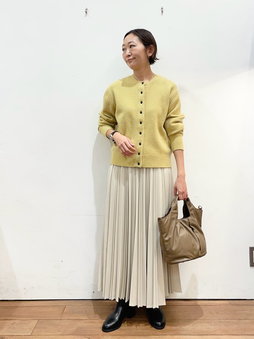 イエロー系のカーディガン/ボレロ、ホワイト系のスカート、ブラック系のブーツを着用したレディースの冬コーディネートの2枚目の写真