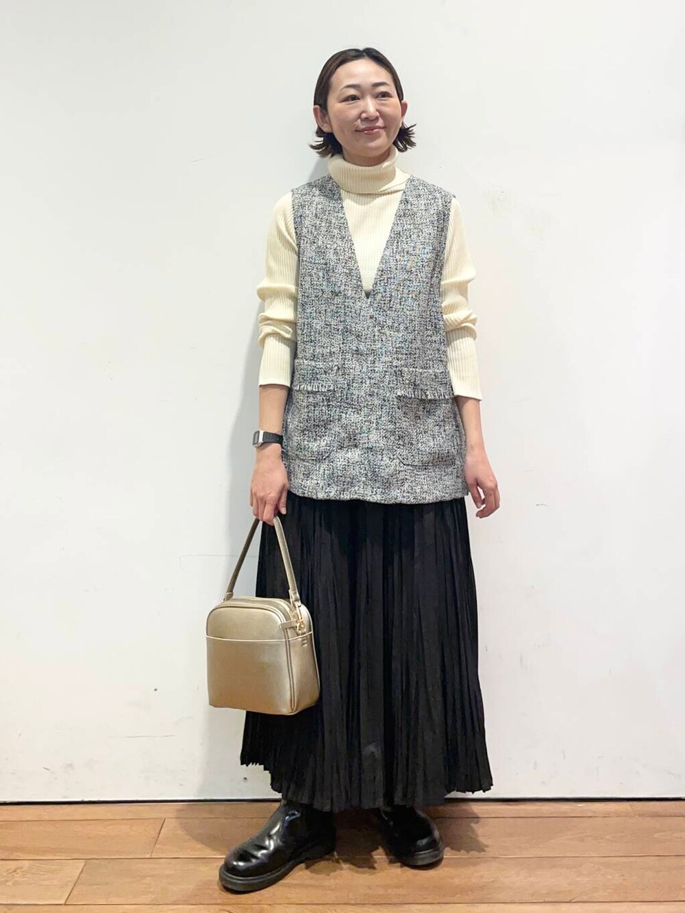 ゴールド系のショルダーバッグ、ホワイト系のニット/セーター、ブラック系のベストを着用したレディースの冬コーディネートの3枚目の写真