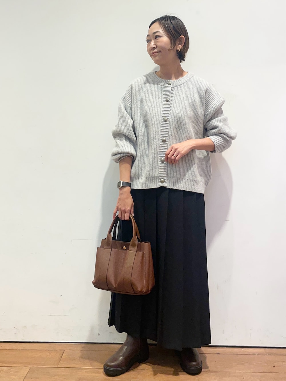 ブラック系のスカート、ブラウン系のトートバッグ、ブラウン系のブーツを着用したレディースの秋コーディネートの2枚目の写真
