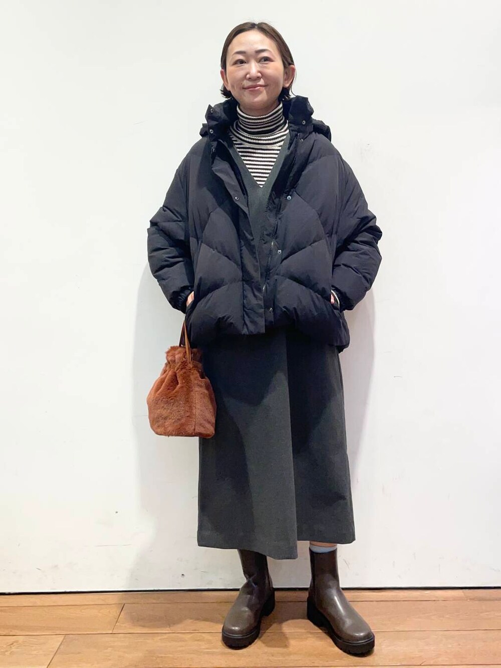 ブラック系のダウンジャケット/コート、グレー系のワンピース、ブラウン系のブーツを着用したレディースの冬コーディネートの2枚目の写真
