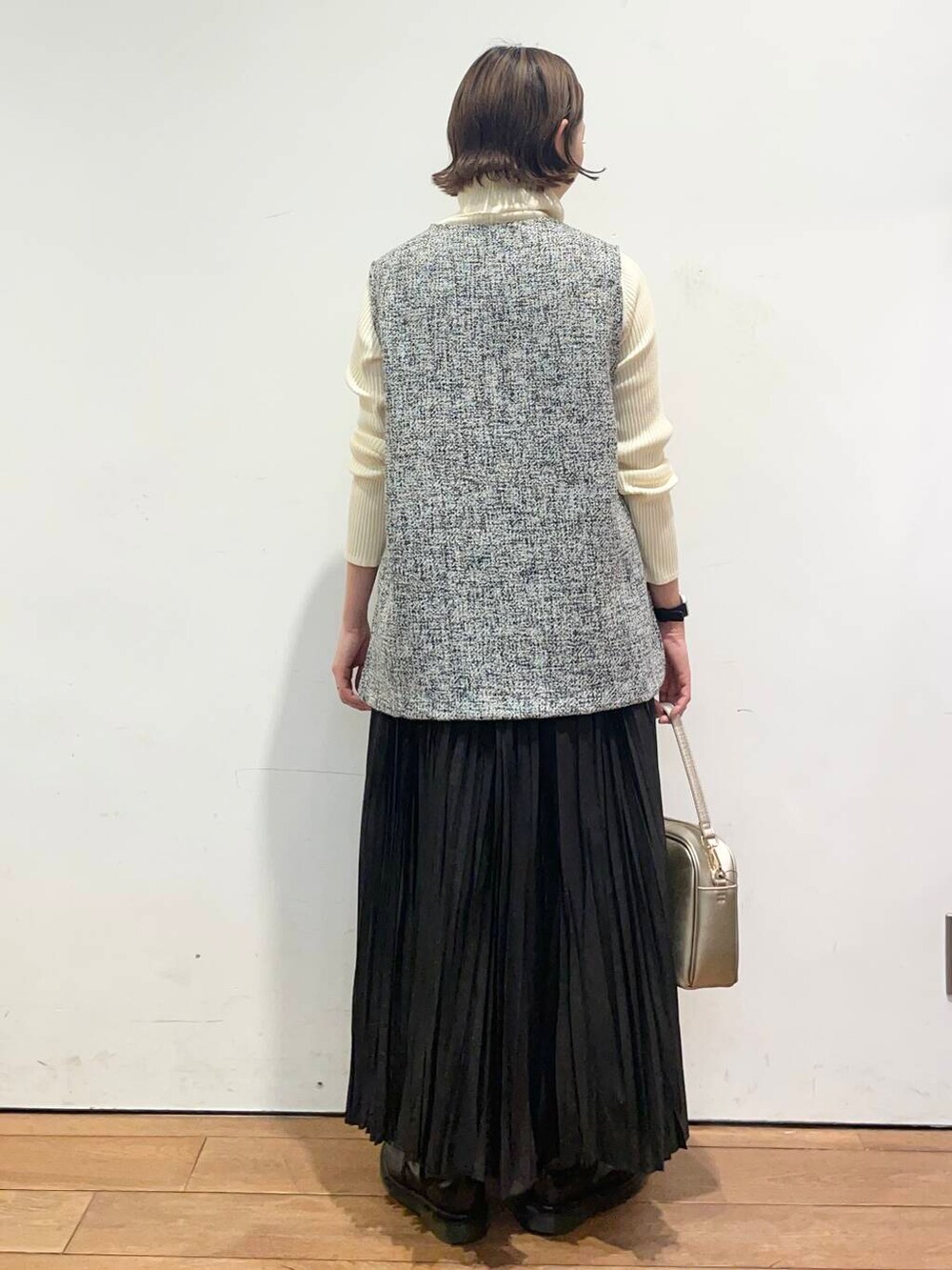 ゴールド系のショルダーバッグ、ホワイト系のニット/セーター、ブラック系のベストを着用したレディースの冬コーディネートの5枚目の写真