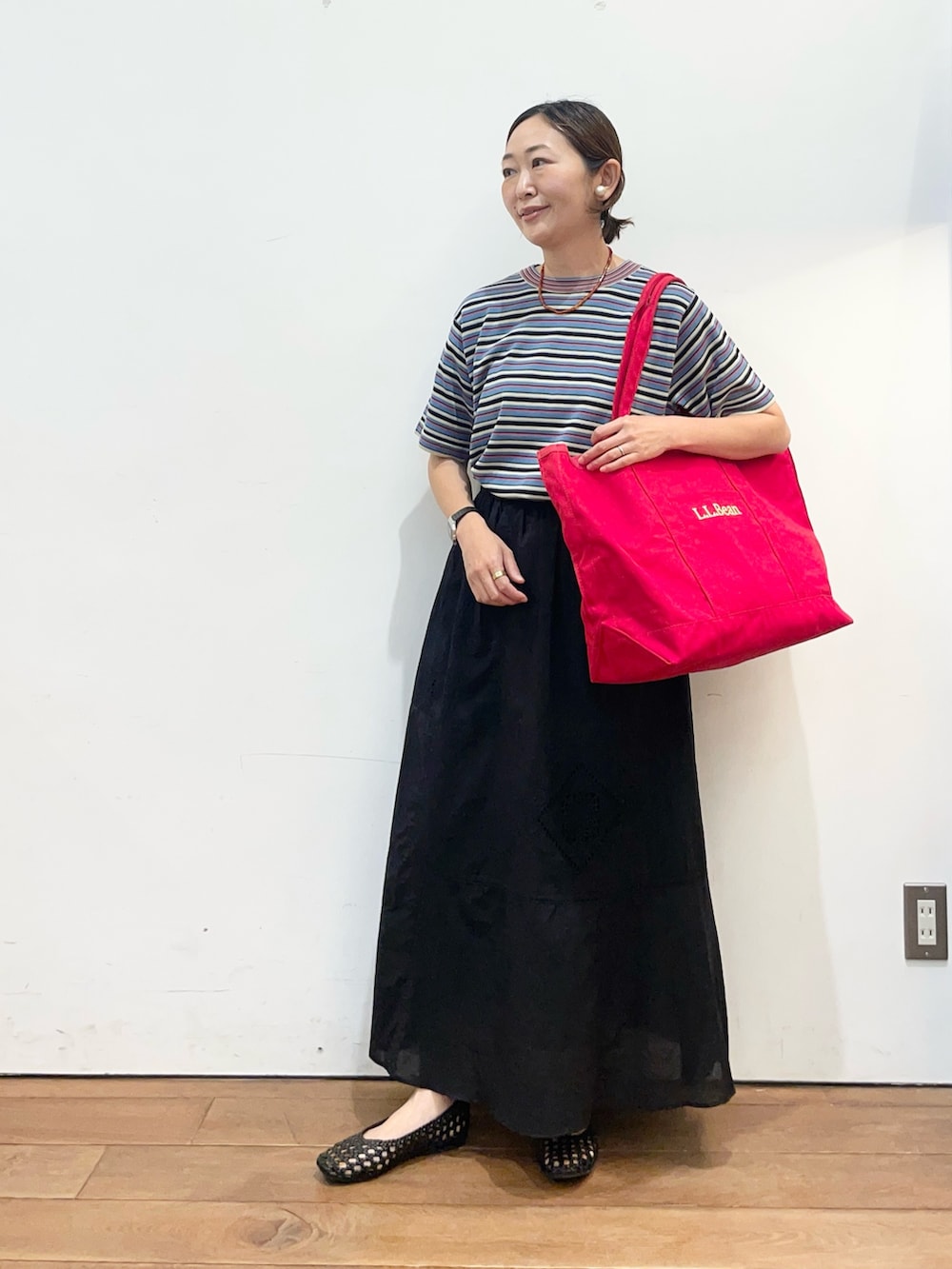 レッド系のトートバッグ、ブラック系のスカート、ブラック系のサンダルを着用したレディースの春コーディネートの3枚目の写真