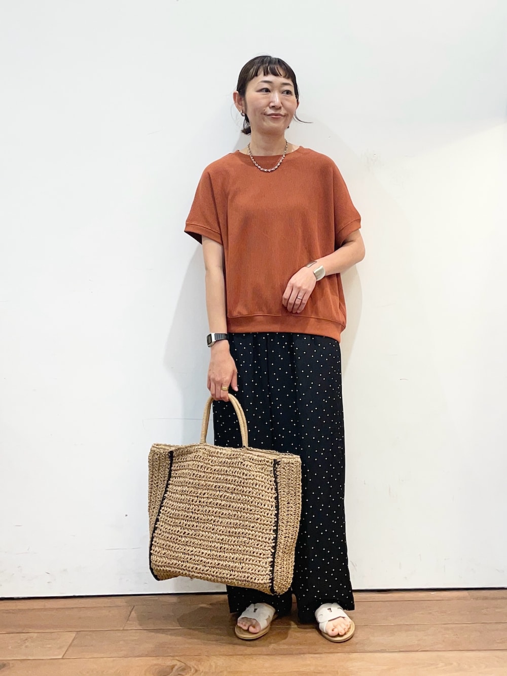 オレンジ系のTシャツ/カットソー、ブラック系のその他パンツ、ベージュ系のトートバッグを着用したレディースの夏コーディネートの2枚目の写真