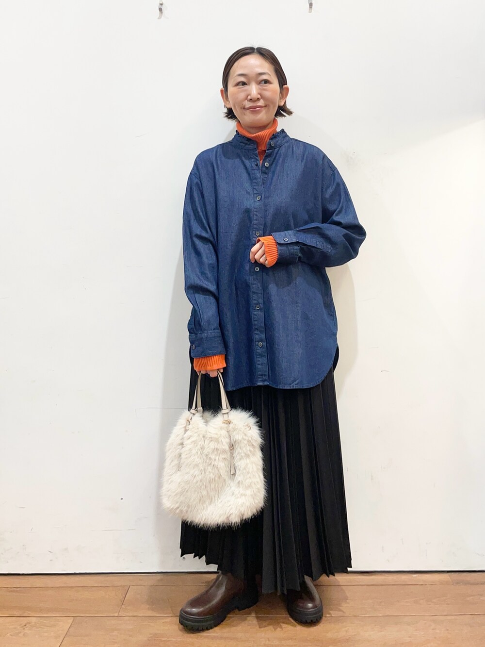 ブルー系のシャツ/ブラウス、オレンジ系のニット/セーター、ブラック系のスカートを着用したレディースの冬コーディネートの2枚目の写真