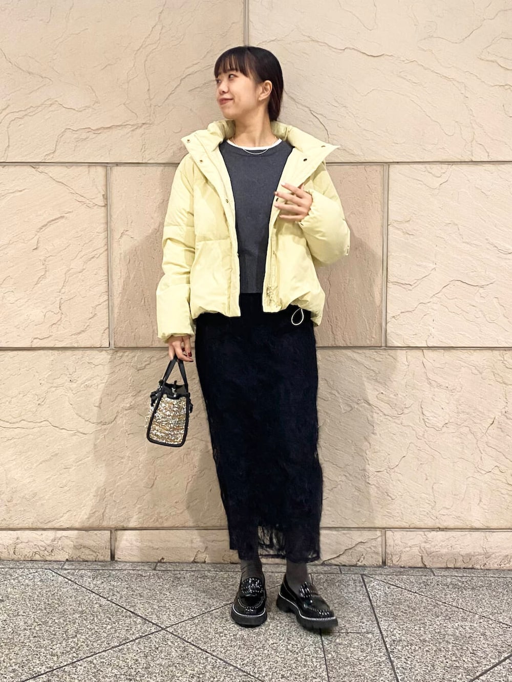 イエロー系のダウンジャケット/コート、グレー系のニット/セーター、イエロー系のハンドバッグを着用したレディースの冬コーディネートの2枚目の写真