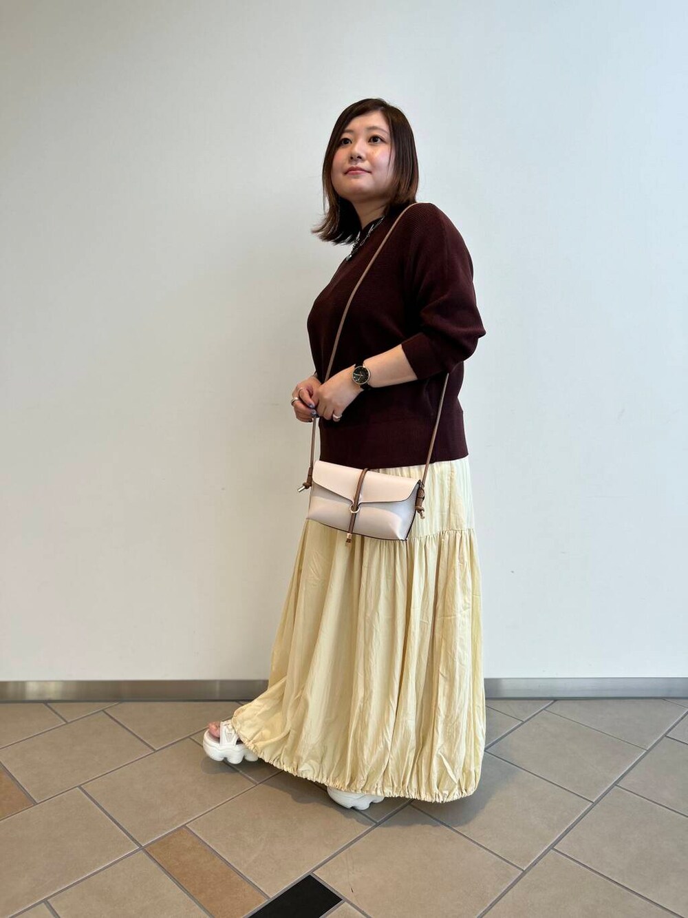 ホワイト系のショルダーバッグ、ブラウン系のニット/セーター、イエロー系のスカートを着用したレディースの夏コーディネートの3枚目の写真