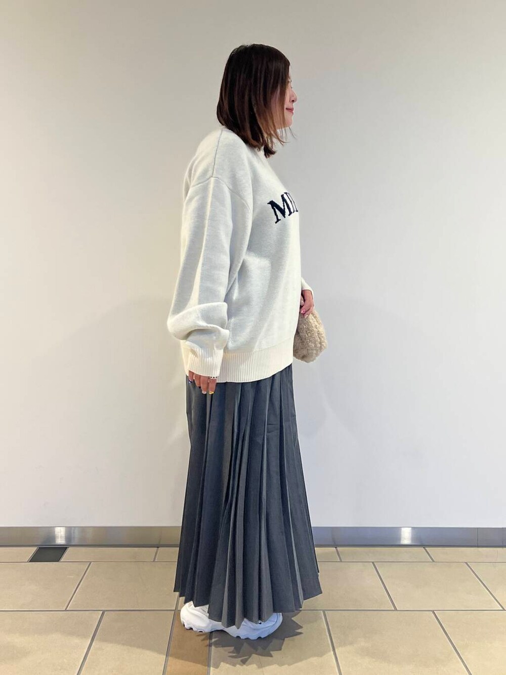 ベージュ系のショルダーバッグ、ホワイト系のニット/セーター、グレー系のスカートを着用したレディースの秋コーディネートの4枚目の写真