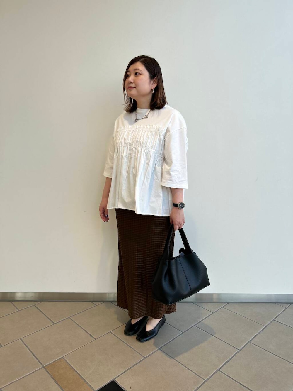 ブラック系のハンドバッグ、ホワイト系のTシャツ/カットソー、ブラウン系のスカートを着用したレディースの夏コーディネートの2枚目の写真
