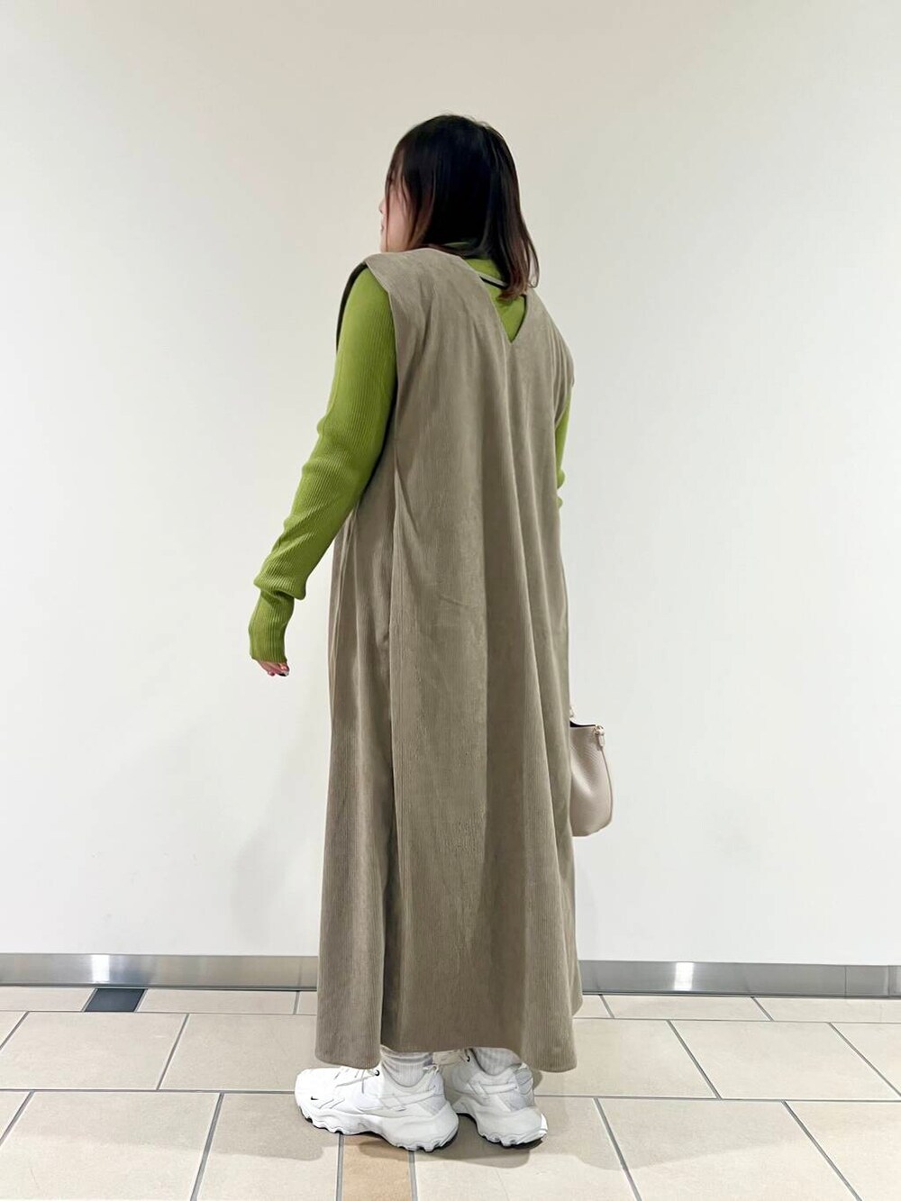 ベージュ系のジャンパースカート、グリーン系のニット/セーター、ホワイト系のショルダーバッグを着用したレディースの秋コーディネートの3枚目の写真