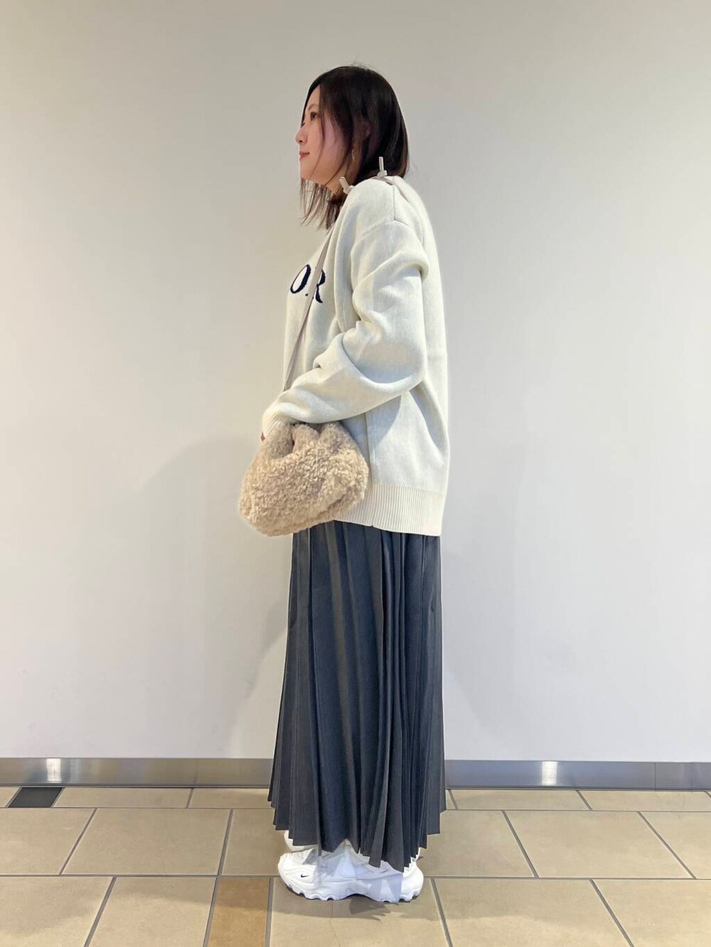 ベージュ系のショルダーバッグ、ホワイト系のニット/セーター、グレー系のスカートを着用したレディースの秋コーディネートの2枚目の写真