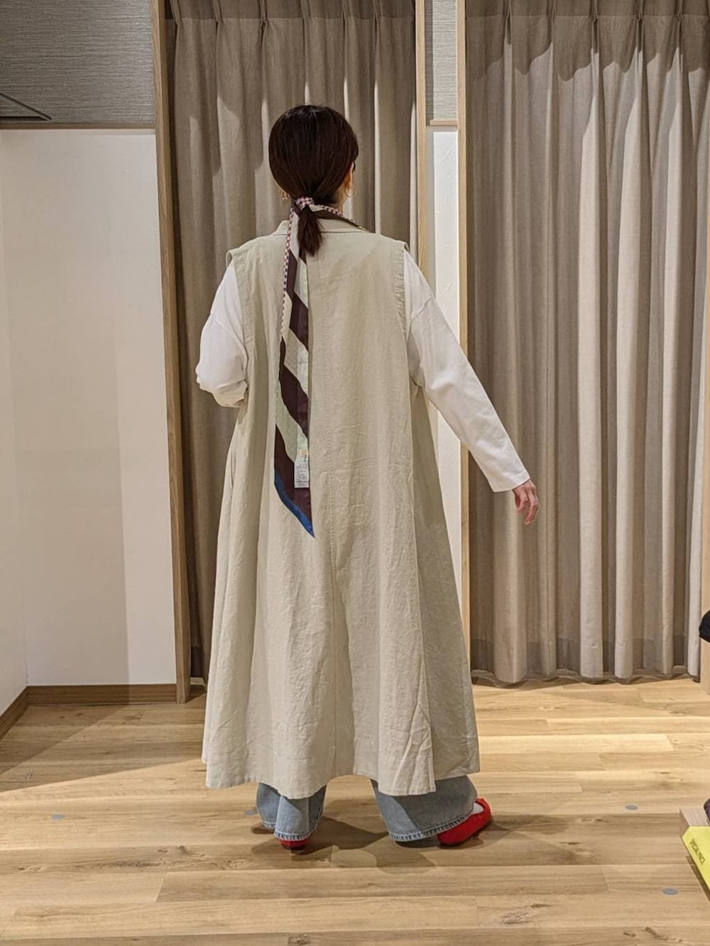 レッド系のパンプス、ブルー系のデニムパンツ、ベージュ系のベストを着用したレディースの冬コーディネートの2枚目の写真