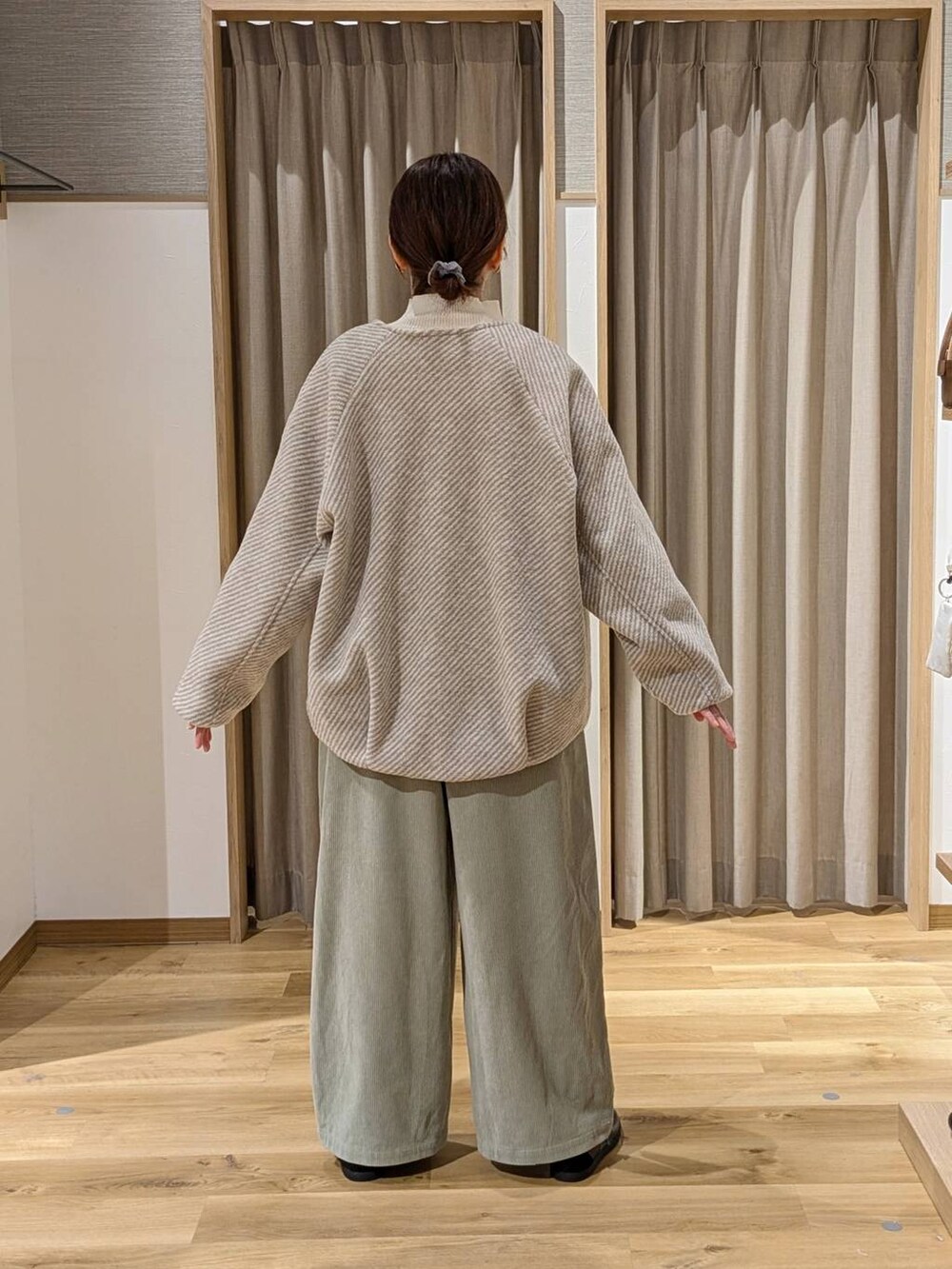 ベージュ系のノーカラーコート、ベージュ系のニット/セーター、ブラック系のスニーカーを着用したレディースの冬コーディネートの3枚目の写真