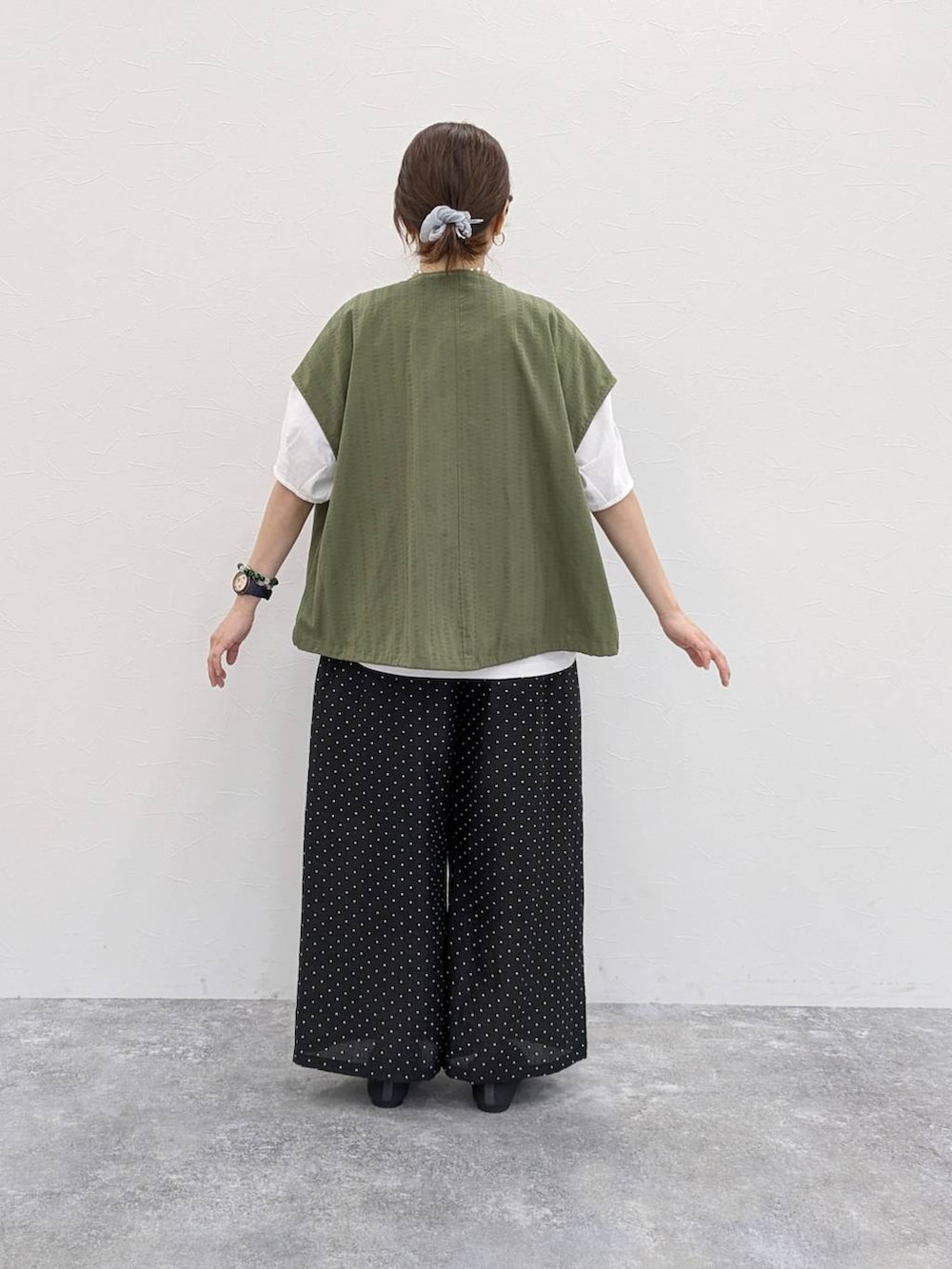 グレー系のパンプス、グリーン系のベスト、グレー系のシュシュを着用したレディースの春コーディネートの2枚目の写真