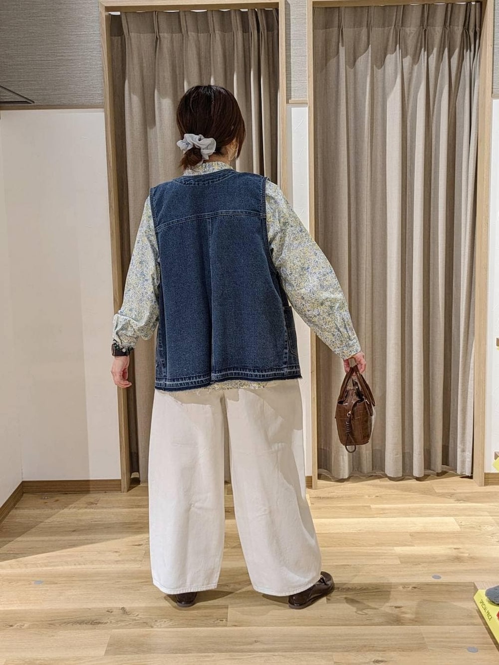 ホワイト系のデニムパンツ、ブルー系のベスト、ブラウン系のトートバッグを着用したレディースの冬コーディネートの2枚目の写真