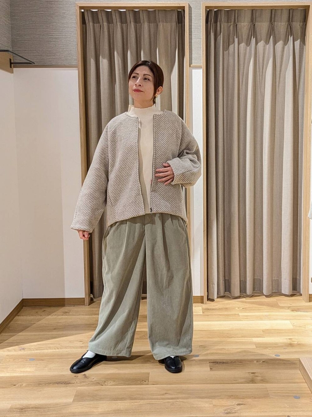 ベージュ系のノーカラーコート、ベージュ系のニット/セーター、ブラック系のスニーカーを着用したレディースの冬コーディネートの2枚目の写真