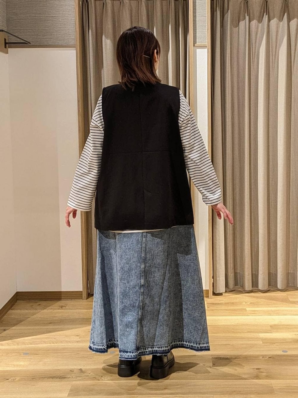 ブラック系のベスト、ブラック系のブーツ、ブルー系のデニムスカートを着用したレディースの冬コーディネートの2枚目の写真