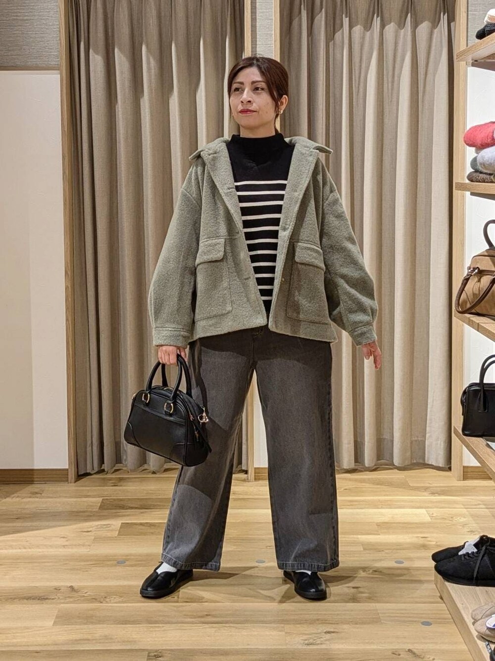 グリーン系のブルゾン、グレー系のデニムパンツ、ブラック系のショルダーバッグを着用したレディースの冬コーディネートの2枚目の写真
