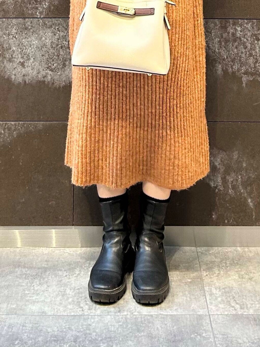 ブラック系のブーツ、ホワイト系のハンドバッグ、オレンジ系のワンピースを着用したレディースの冬コーディネートの5枚目の写真