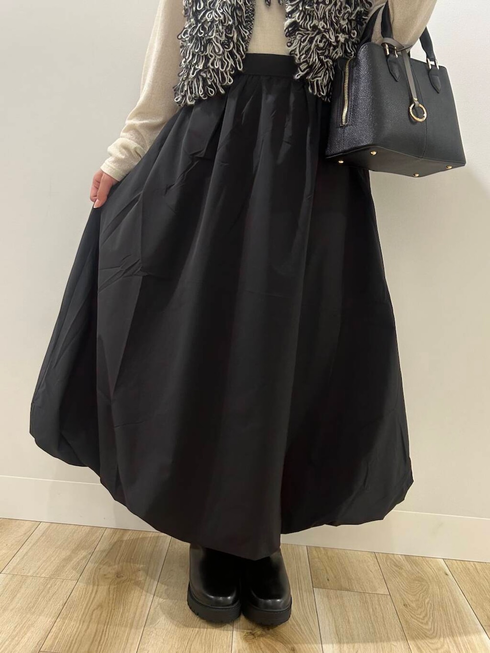 ブラック系のベスト、ブラック系のスカート、ブラック系のブーツを着用したレディースの秋コーディネートの5枚目の写真