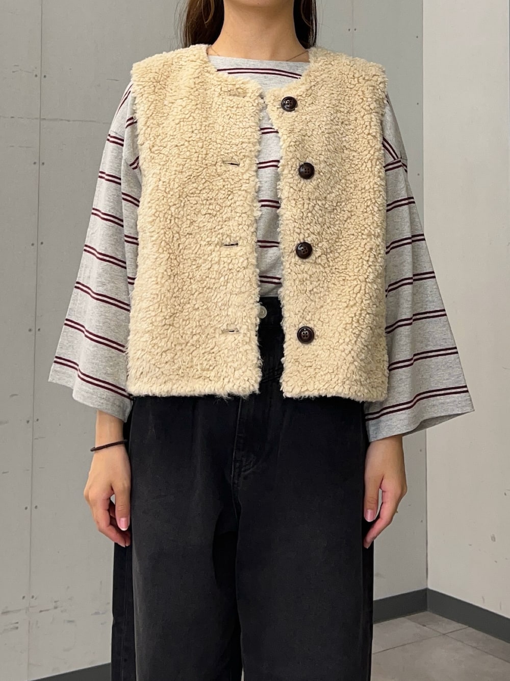 グレー系のTシャツ/カットソー、ベージュ系のダウンベスト、ブラック系のデニムパンツを着用したレディースの秋コーディネートの4枚目の写真