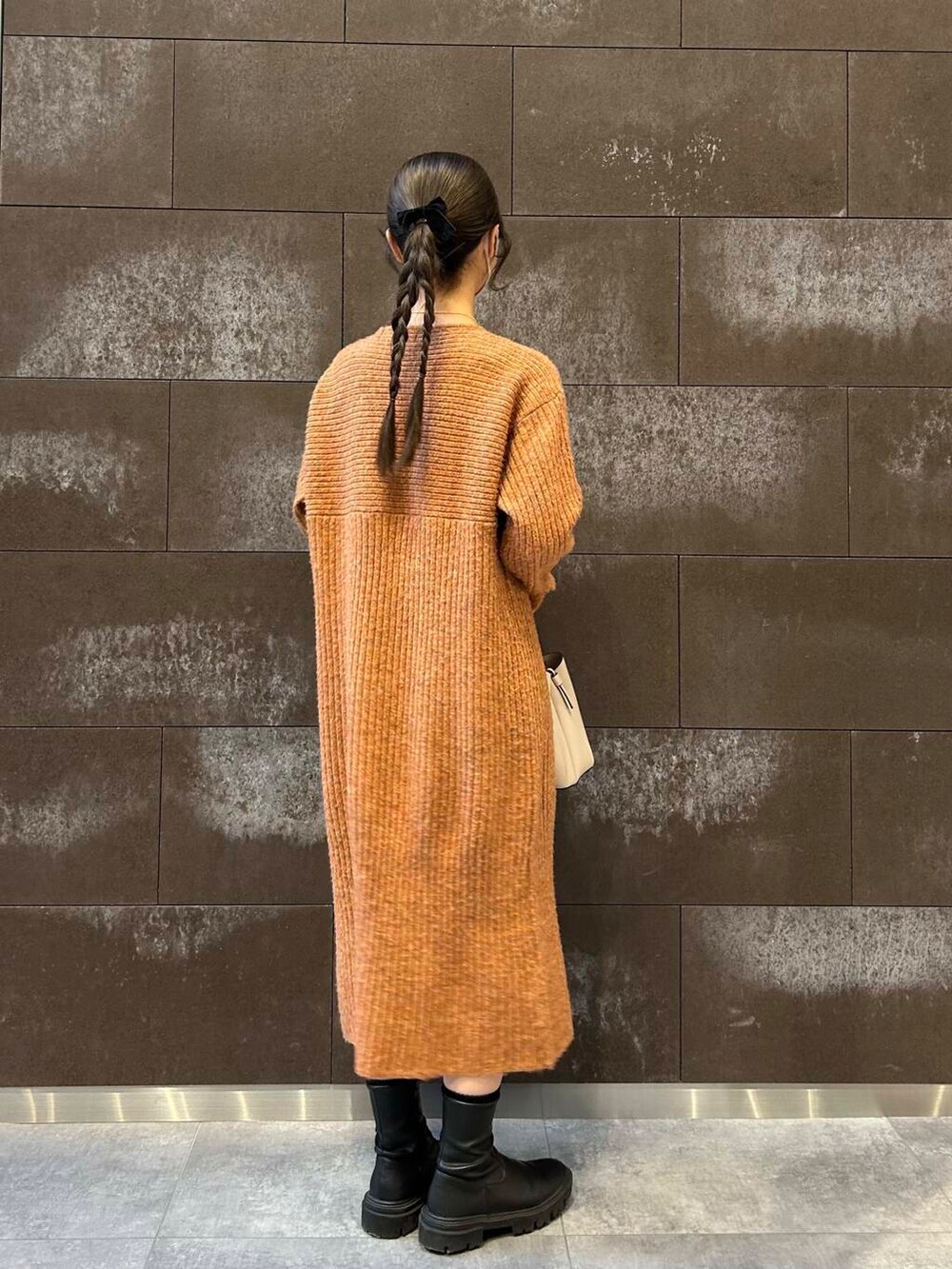 ブラック系のブーツ、ホワイト系のハンドバッグ、オレンジ系のワンピースを着用したレディースの冬コーディネートの2枚目の写真