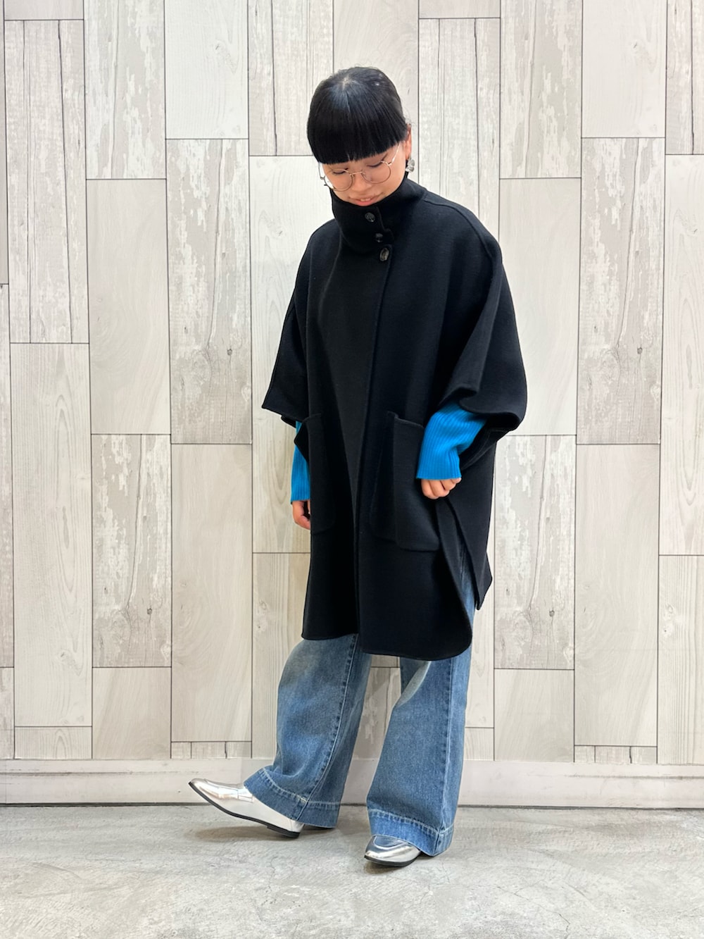 ブラック系のニット/セーター、ブラック系のポンチョ、ブルー系のデニムパンツを着用したレディースの秋コーディネートの4枚目の写真