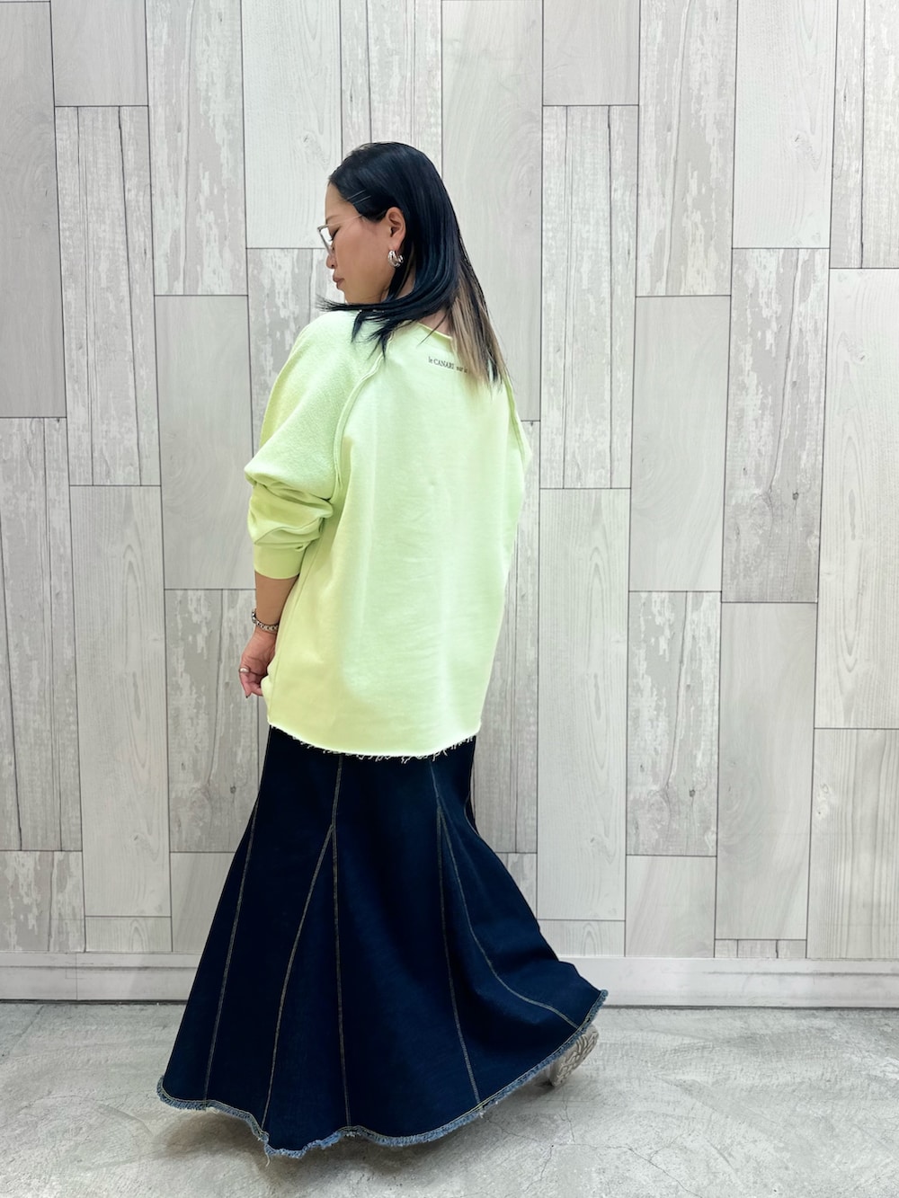 グリーン系のスウェット、ブルー系のデニムスカート、ホワイト系のスニーカーを着用したレディースの春コーディネートの3枚目の写真