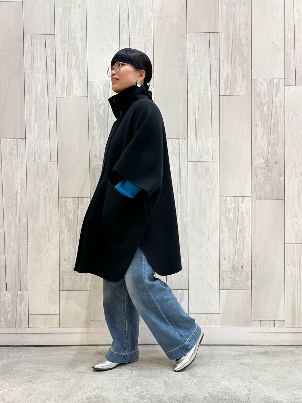 ブラック系のニット/セーター、ブラック系のポンチョ、ブルー系のデニムパンツを着用したレディースの秋コーディネートの3枚目の写真