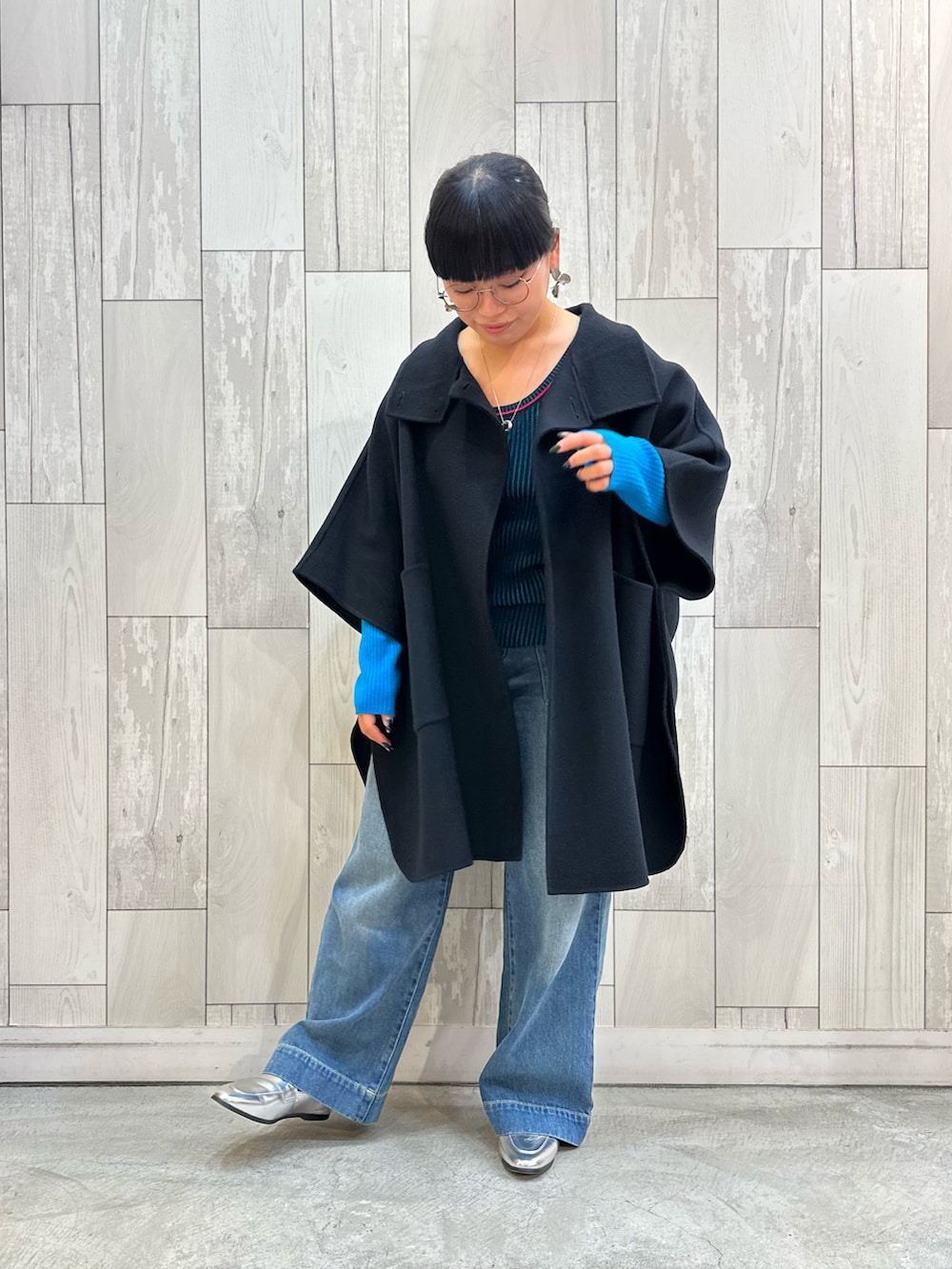 ブラック系のニット/セーター、ブラック系のポンチョ、ブルー系のデニムパンツを着用したレディースの秋コーディネートの2枚目の写真