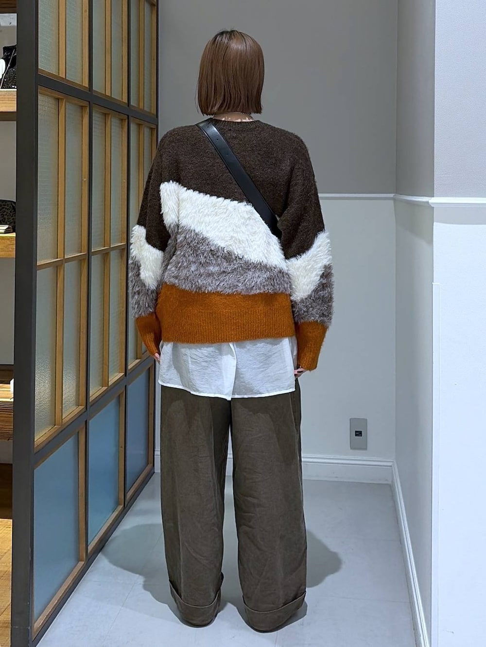 ブラック系のショルダーバッグ、ホワイト系のTシャツ/カットソー、ブラウン系のニット/セーターを着用したレディースの冬コーディネートの3枚目の写真