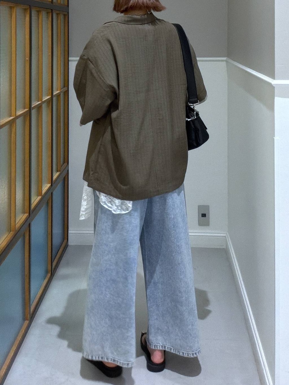 ブラック系のショルダーバッグ、ブルー系のデニムパンツ、ブラック系のサンダルを着用したレディースの春コーディネートの2枚目の写真