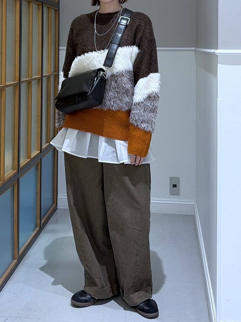 ブラック系のショルダーバッグ、ホワイト系のTシャツ/カットソー、ブラウン系のニット/セーターを着用したレディースの冬コーディネートの2枚目の写真