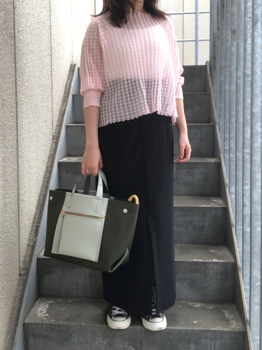 グリーン系のハンドバッグ、ピンク系のニット/セーター、ブラック系のスカートを着用したレディースの秋コーディネートの2枚目の写真