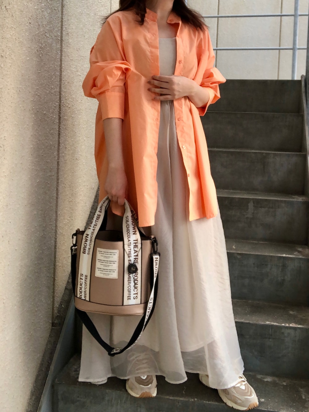 オレンジ系のシャツ/ブラウス、ベージュ系のワンピース、ベージュ系のショルダーバッグを着用したレディースの秋コーディネートの2枚目の写真