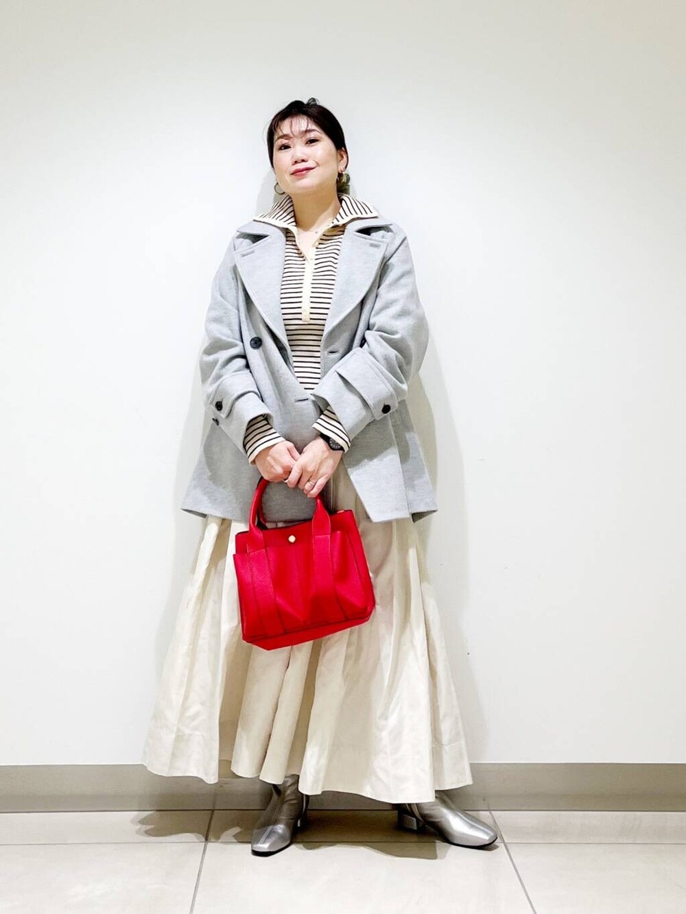 グレー系のピーコート、レッド系のトートバッグ、ホワイト系のニット/セーターを着用したレディースの秋コーディネートの2枚目の写真